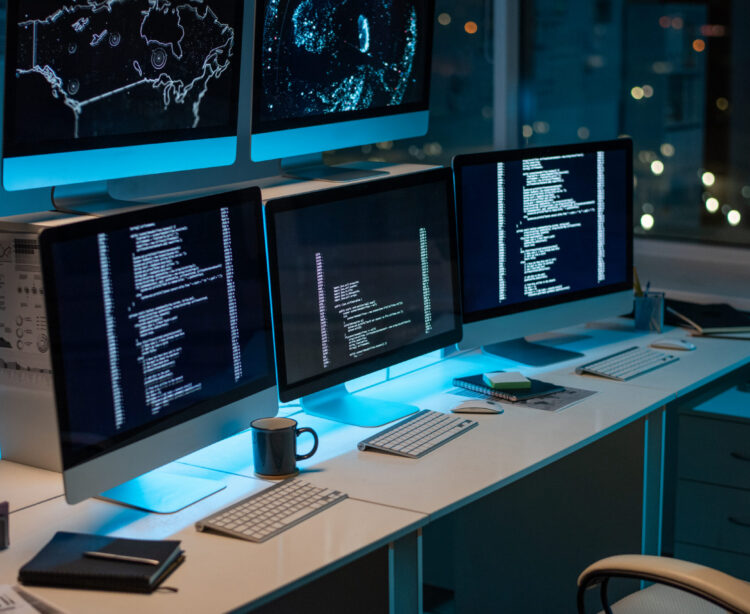 Workplace of contemporary it-engineers with three computers standing on desk in large openspace office